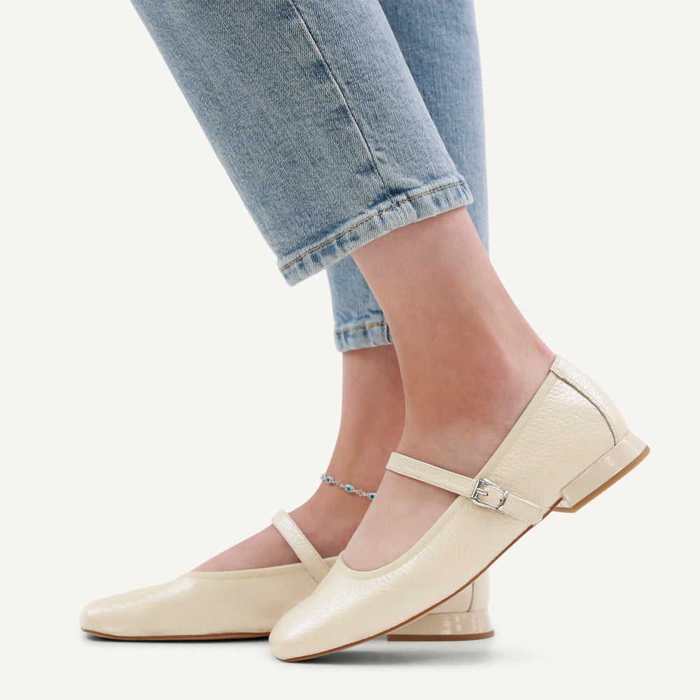 Beige flat shoes worn with light blue jeans on a white background