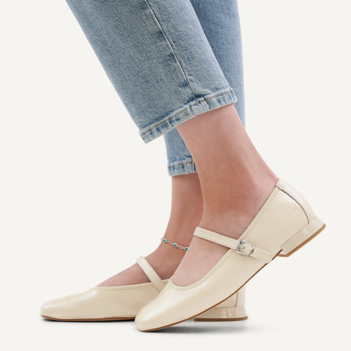 Beige flat shoes worn with light blue jeans on a white background