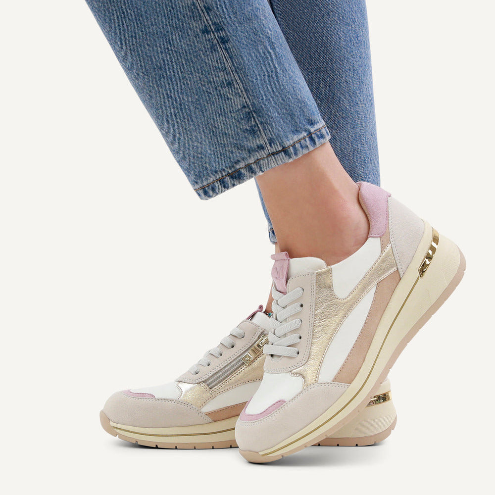 Close-up of beige and white sneakers with pink accents worn with blue jeans on a white background