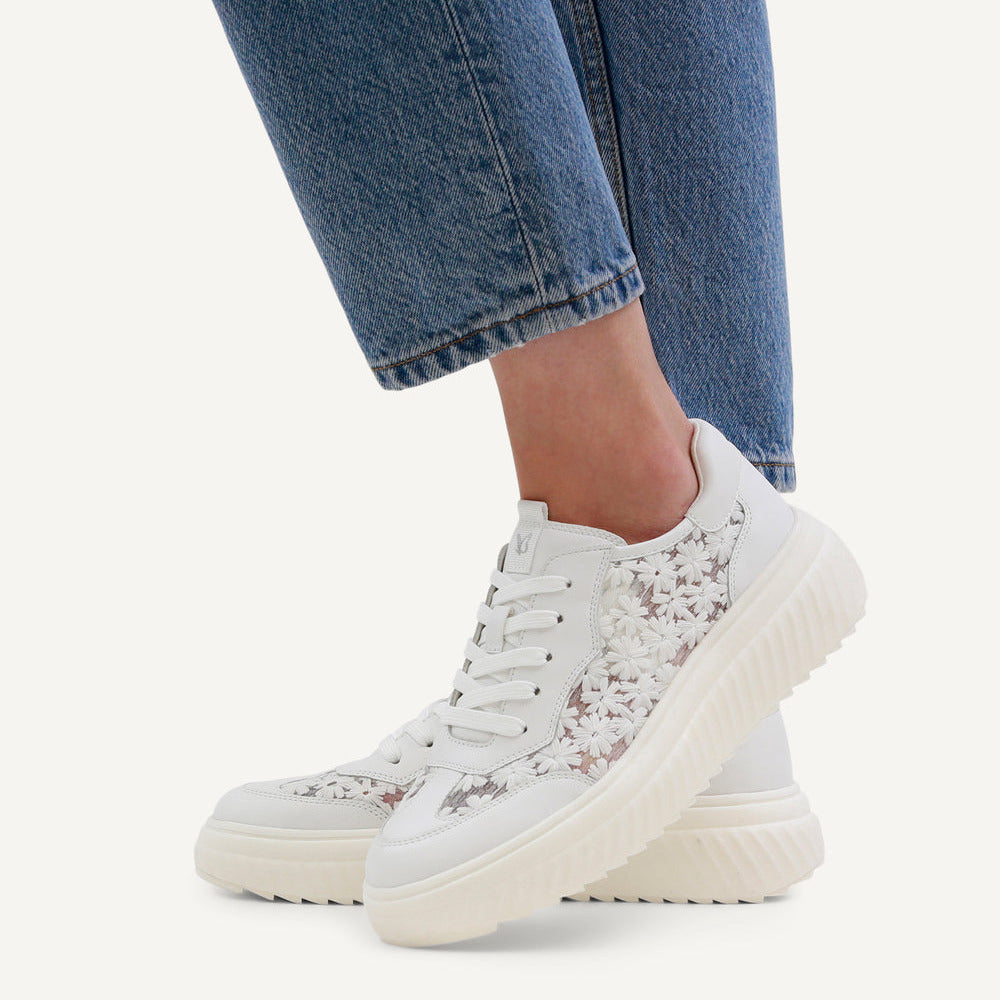 White floral sneakers worn with blue jeans on a white background