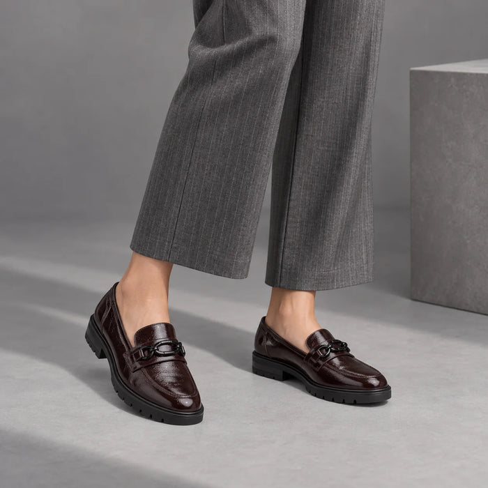 Ara Cambridge merlot patent loafers worn with grey pinstripe trousers and bare ankles in a grey studio.