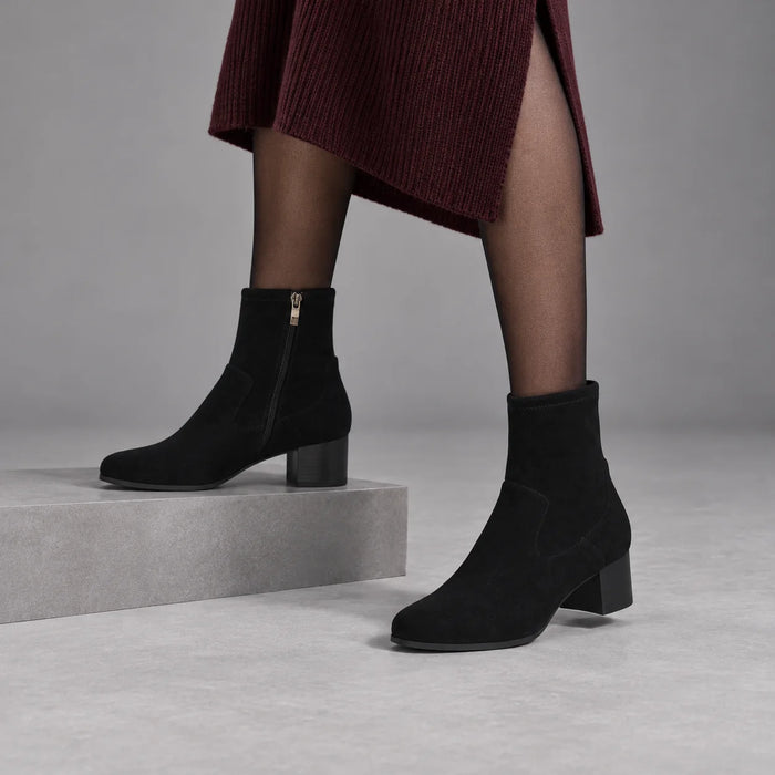 Caprice black stretch ankle boots styled with sheer tights and a burgundy skirt in a grey studio.