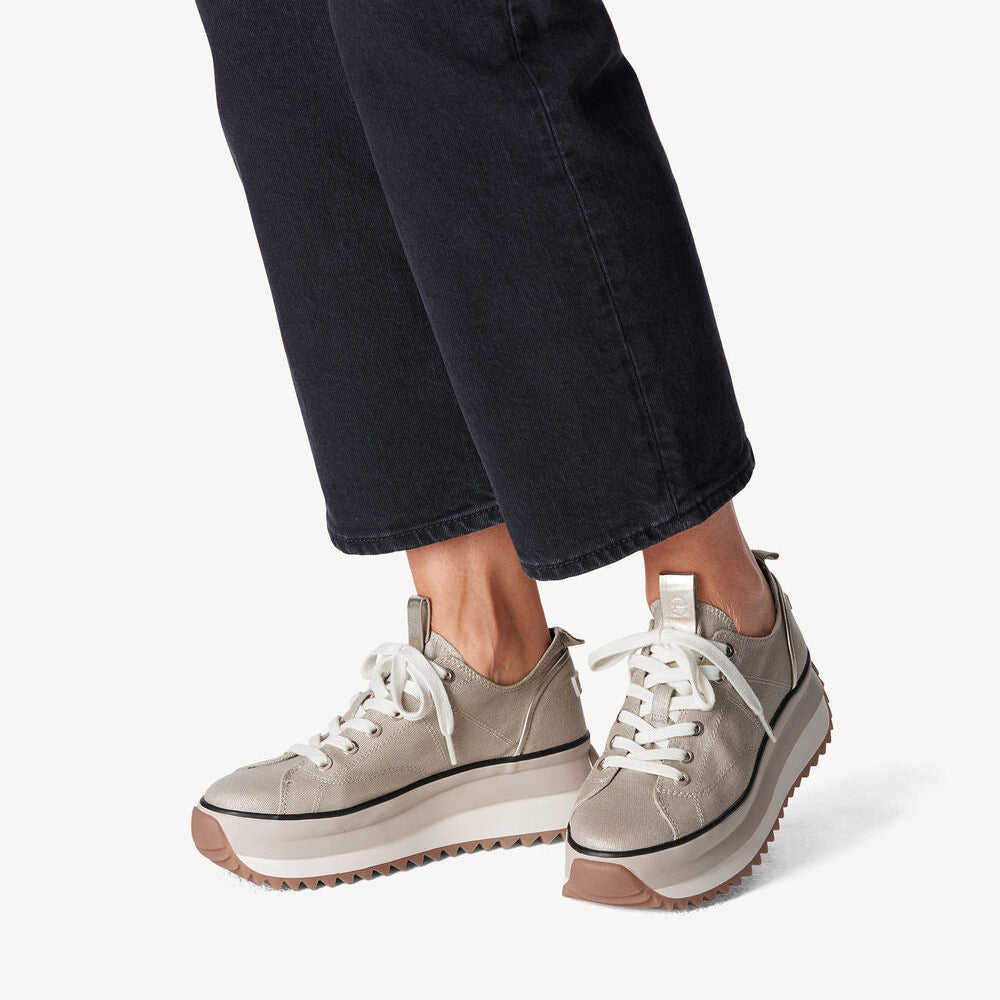 Beige sneakers worn with dark jeans on a white background