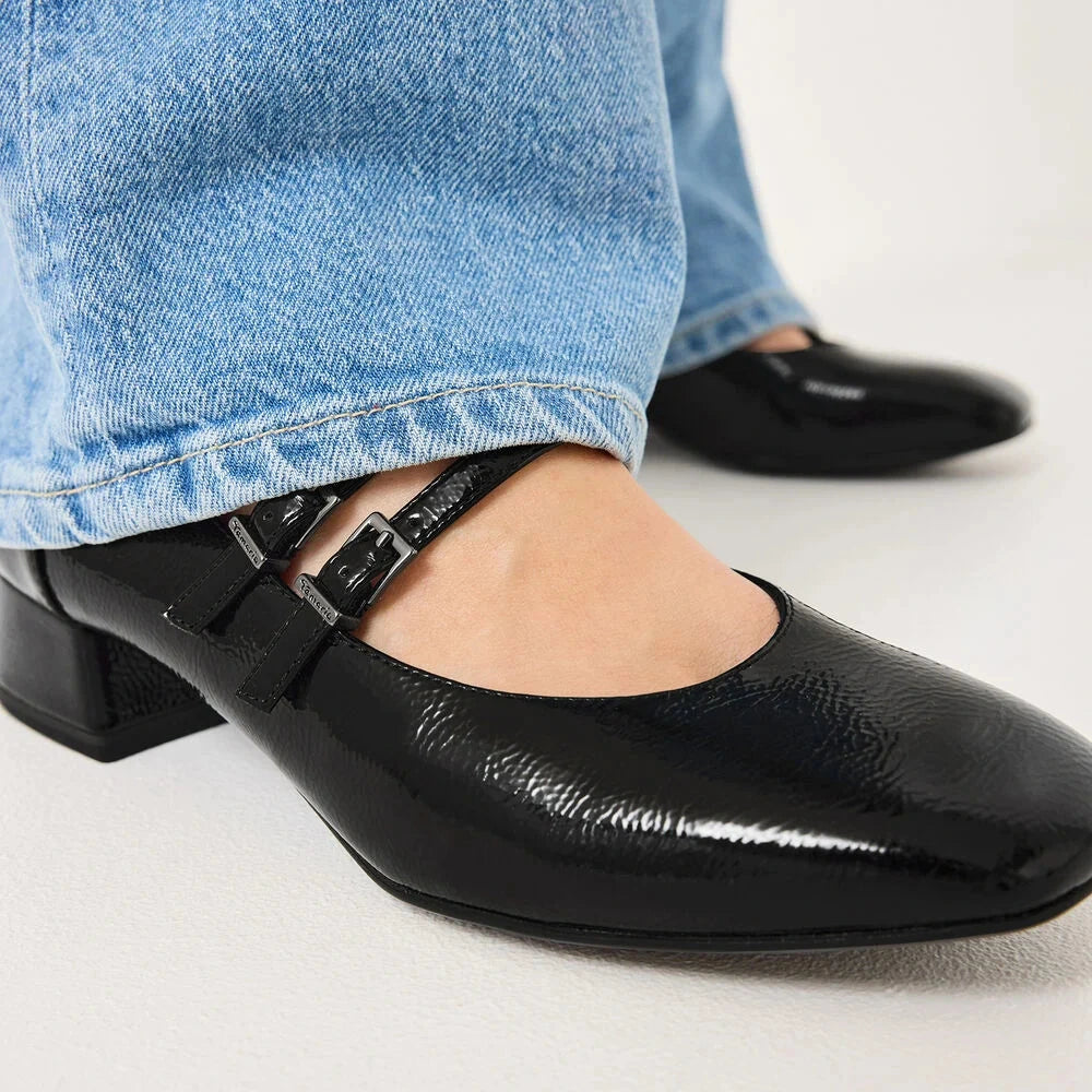 Black patent leather shoes worn with light blue jeans on a white background