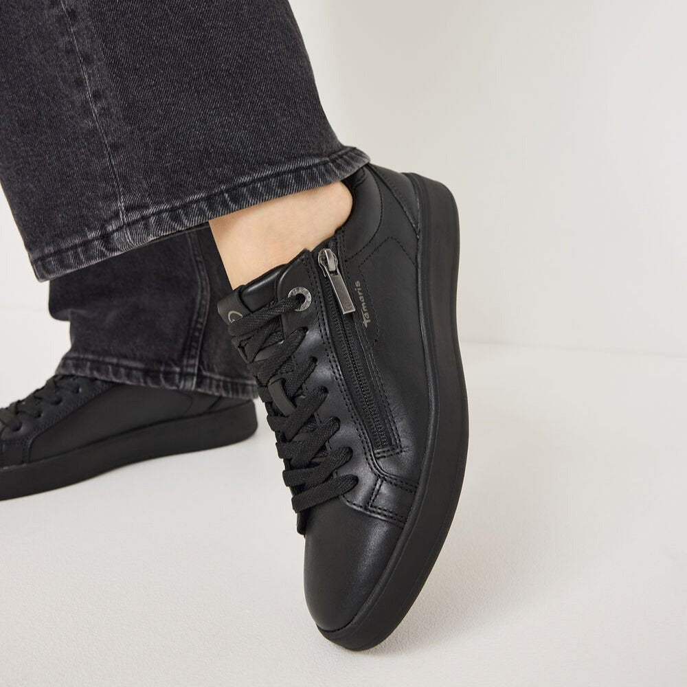 Black sneakers worn with black jeans on a light gray background