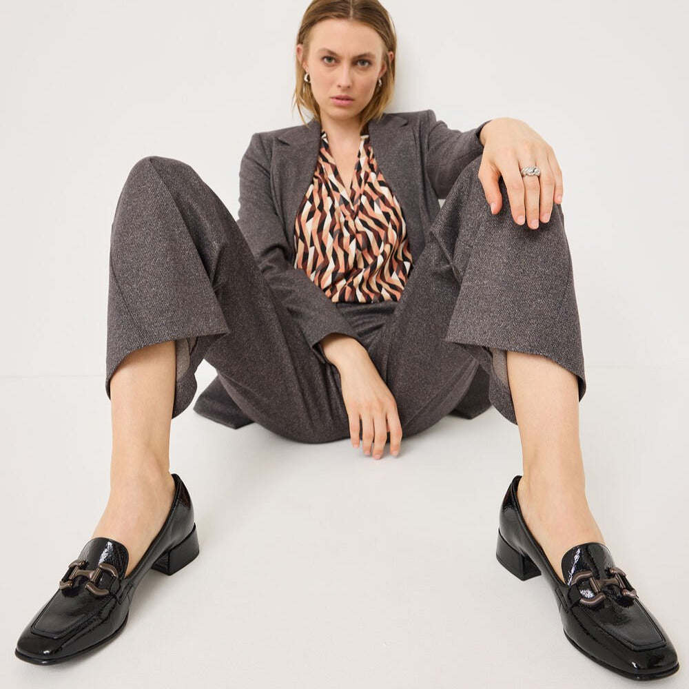 Woman sitting on a white floor wearing a gray outfit with a patterned top.