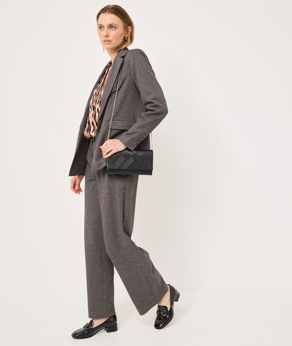 A woman models a gray two-piece suit with wide-leg trousers, paired with a leopard-print top, black loafers, and a black quilted shoulder bag, set against a plain white studio background.