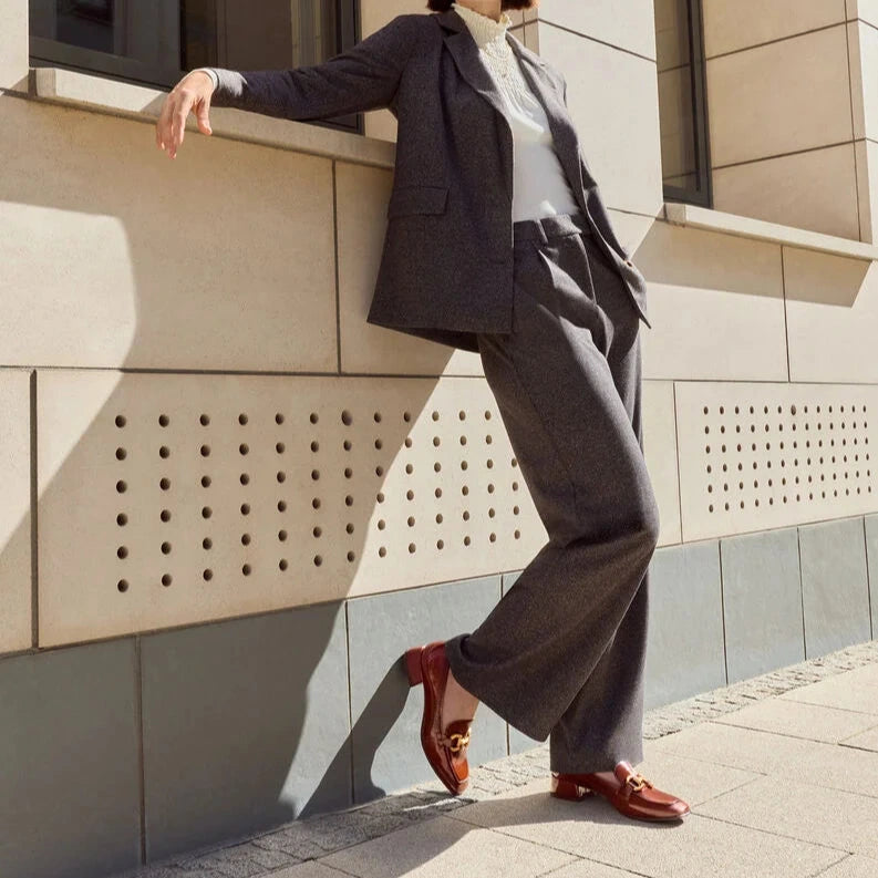 Woman in a gray suit leaning against a modern building.