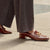 Brown loafers with gold accents worn with gray trousers on a pavement.