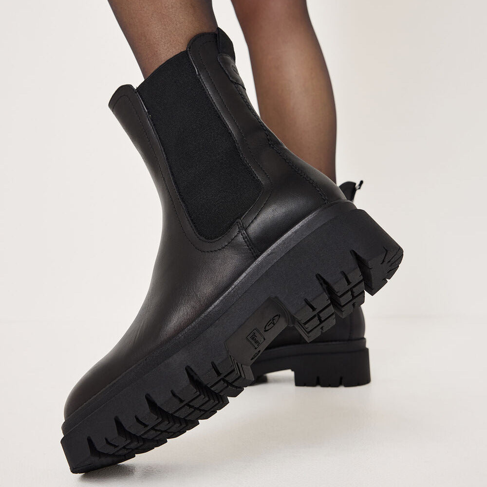 Black Chelsea-style ankle boots with elastic side panels and chunky lug soles, shown on a model against a plain light background.