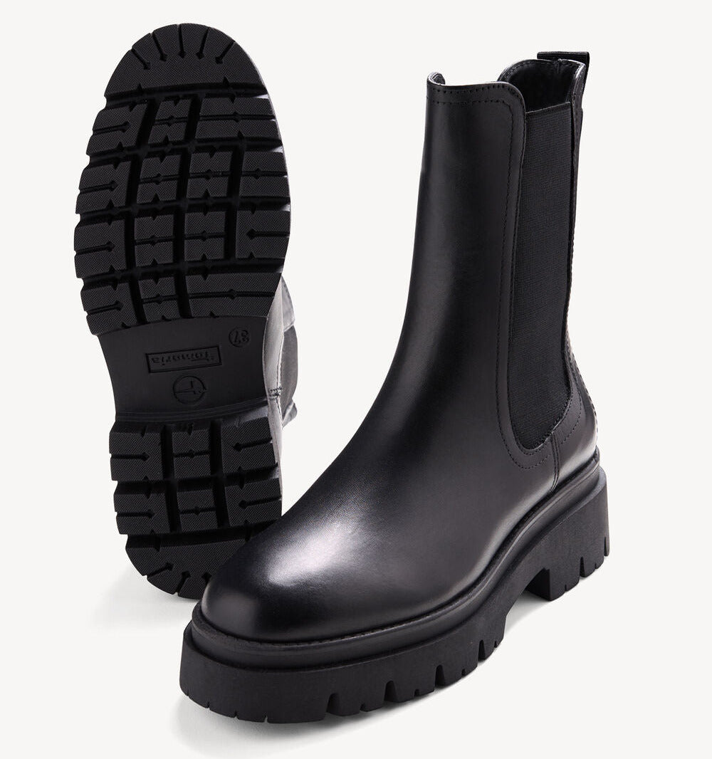 A pair of black Chelsea-style boots with chunky lug soles, shown on a clean white background. One boot is positioned upright to show the side profile, while the other is turned to display the treaded outsole.