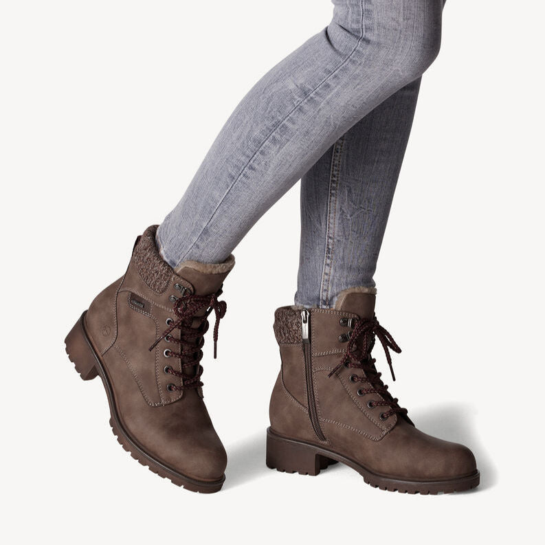 Brown lace-up boots worn with light blue jeans on a white background