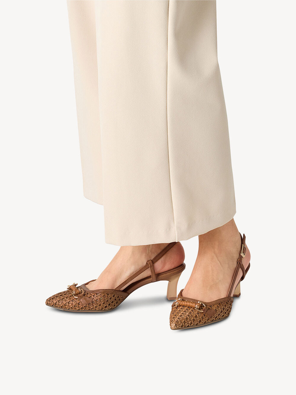 Brown pointed-toe shoes worn with beige pants on a white background