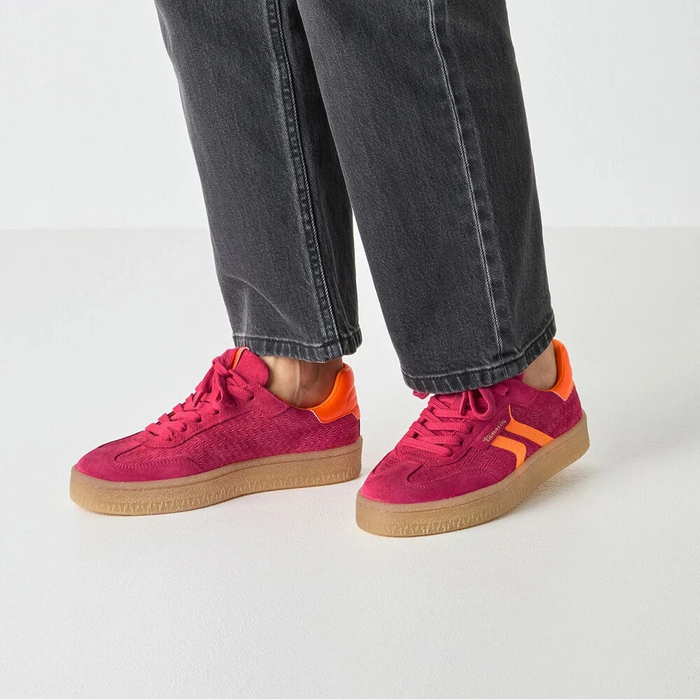 Person wearing bright pink sneakers with orange accents and gum soles on a white background