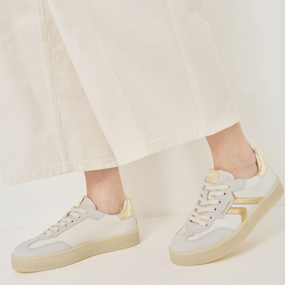 White sneakers with yellow accents worn by a person on a light background