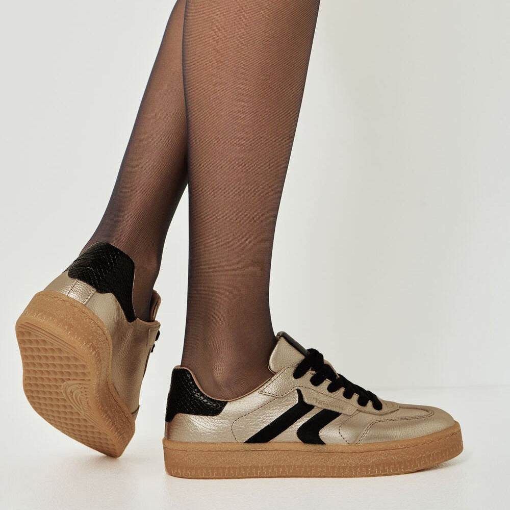 Beige sneakers with black accents worn by a person on a plain background