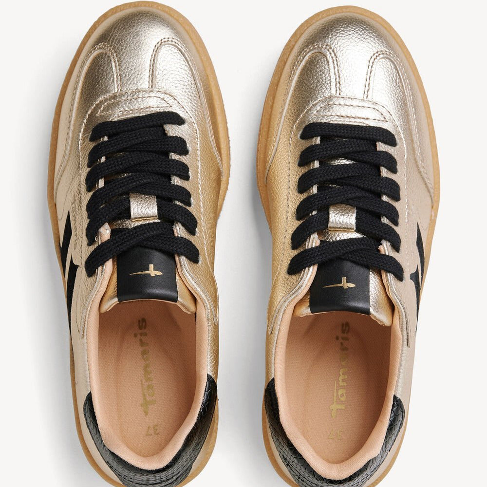 Pair of gold sneakers with black laces on a white background