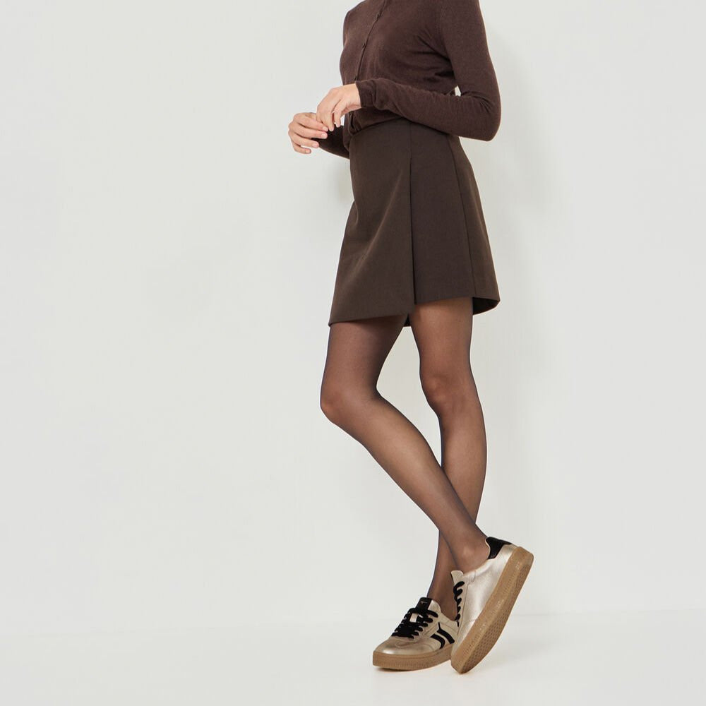 Woman wearing a brown dress and black tights against a white background