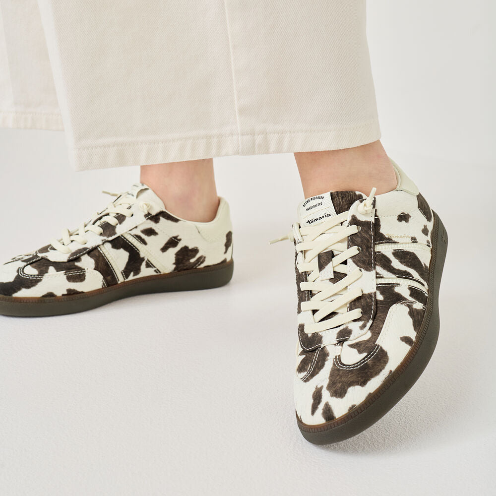 Cow print sneakers worn with white pants on a light gray background
