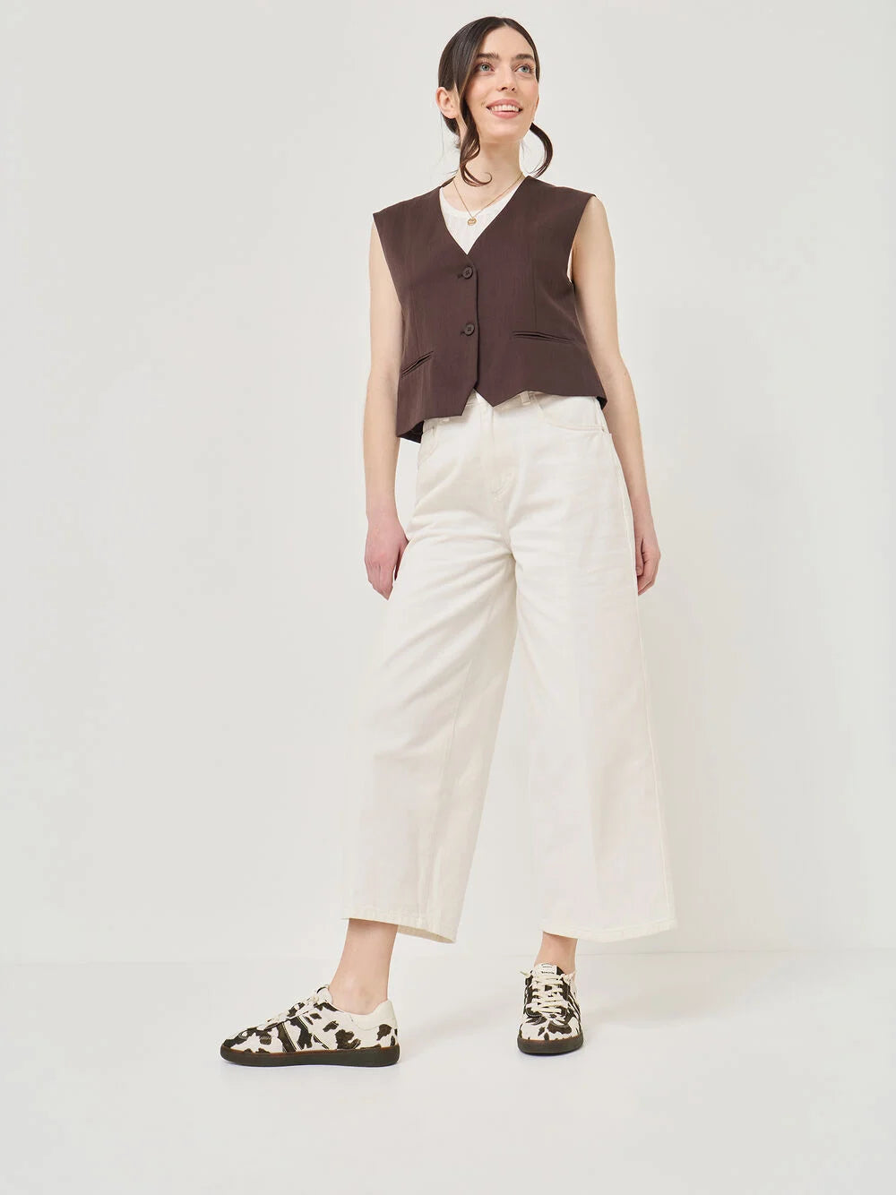 Person wearing a brown sleeveless top and white pants on a white background