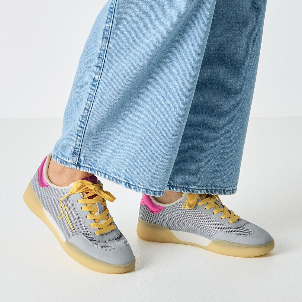 Gray sneakers with yellow laces worn with light blue jeans on a white background