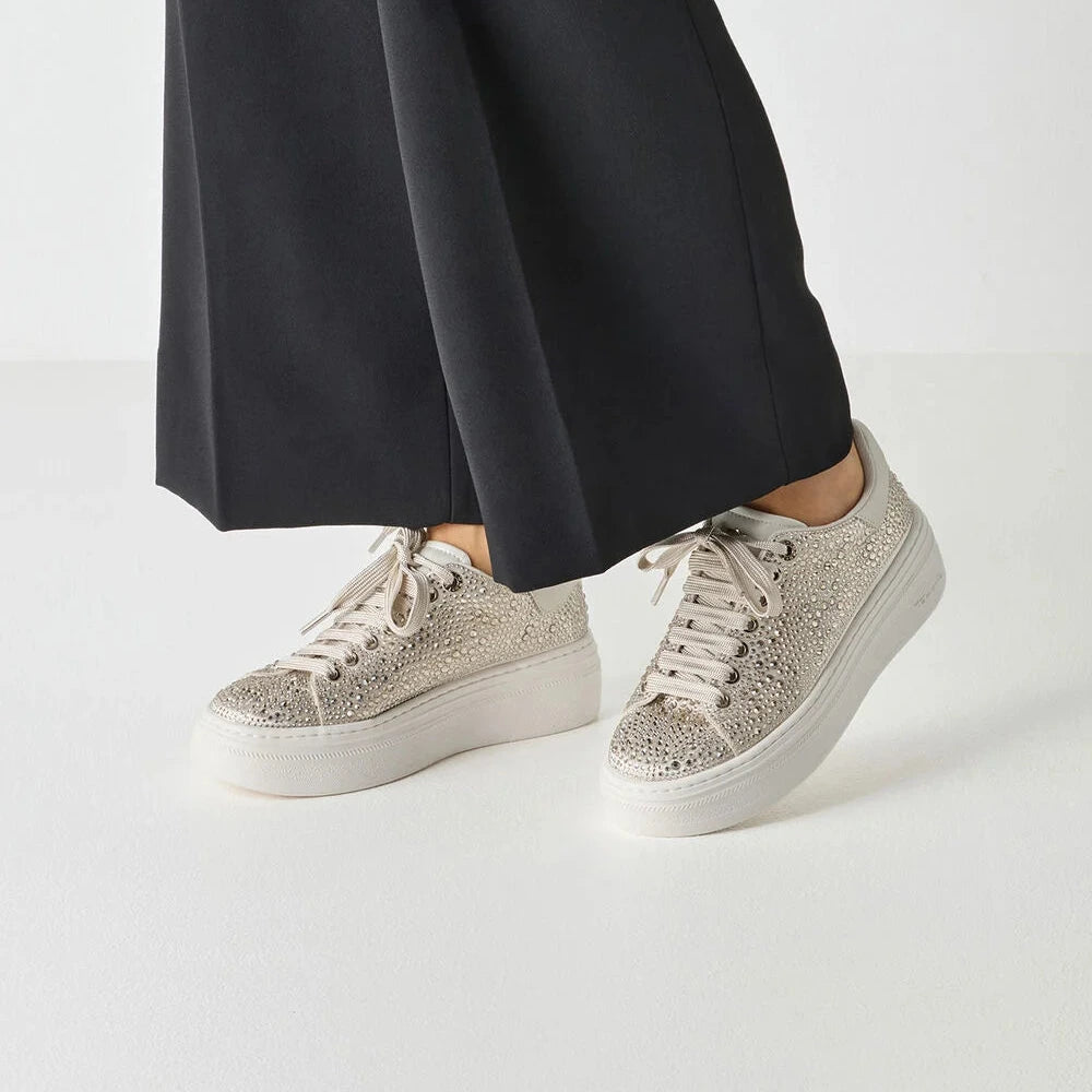 White sneakers with rhinestone embellishments worn with black pants on a white background
