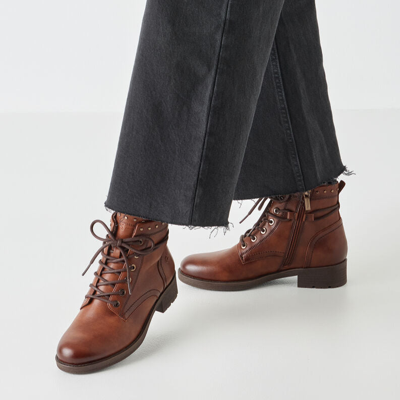 Brown lace-up boots worn with black pants on a white background