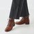 Brown lace-up boots worn with black pants on a white background