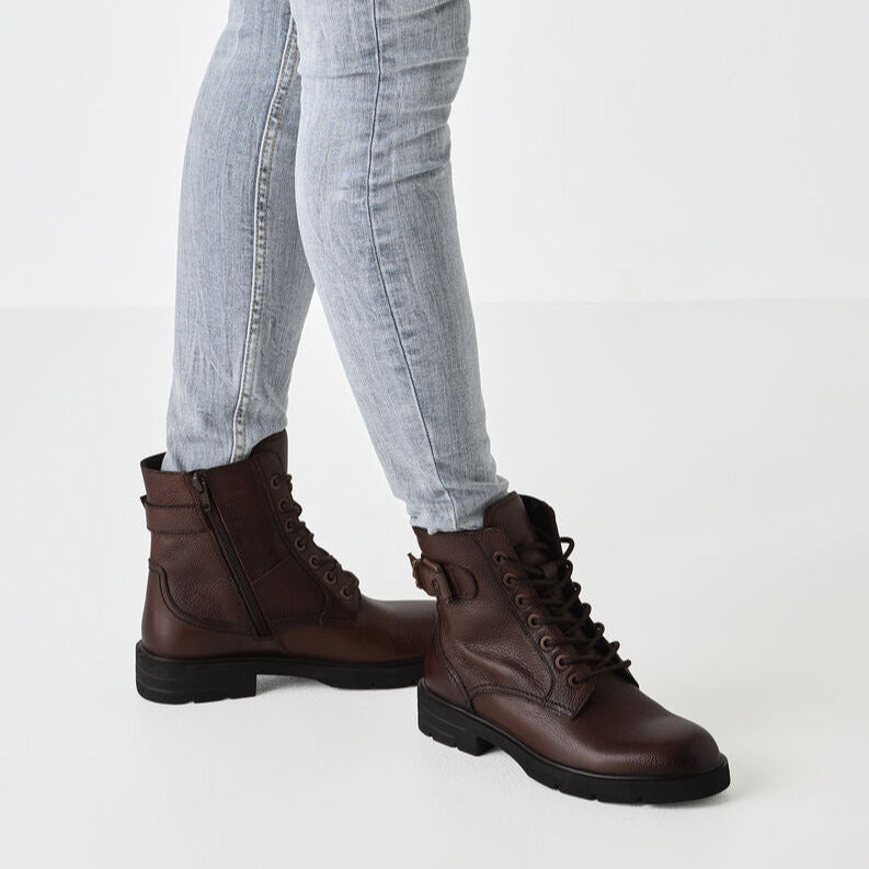 Brown leather boots worn with light blue jeans on a white background