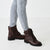 Brown leather boots worn with light blue jeans on a white background