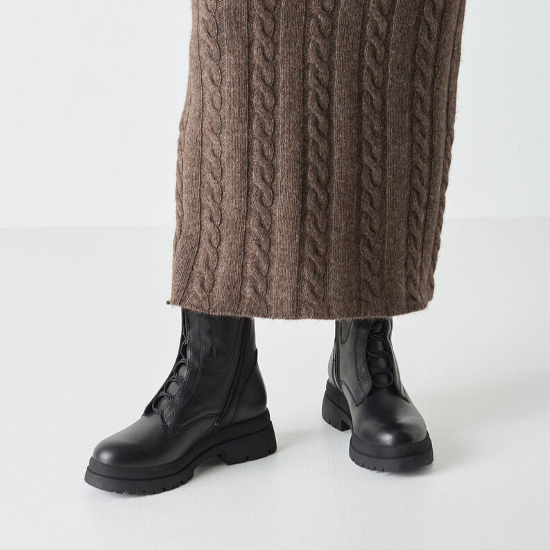 Black boots worn with a brown cable-knit skirt on a white background
