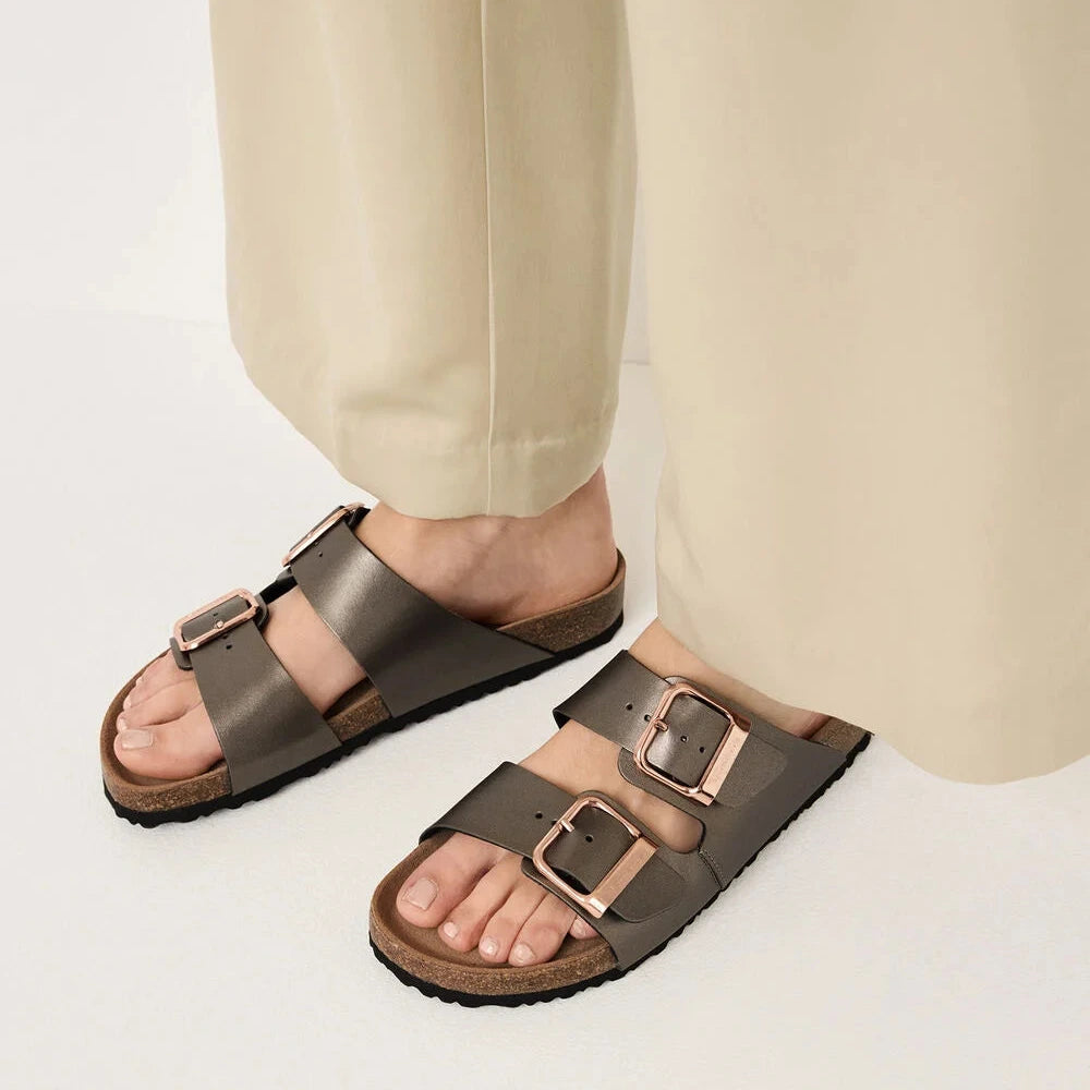 Person wearing brown sandals with buckles on a light background