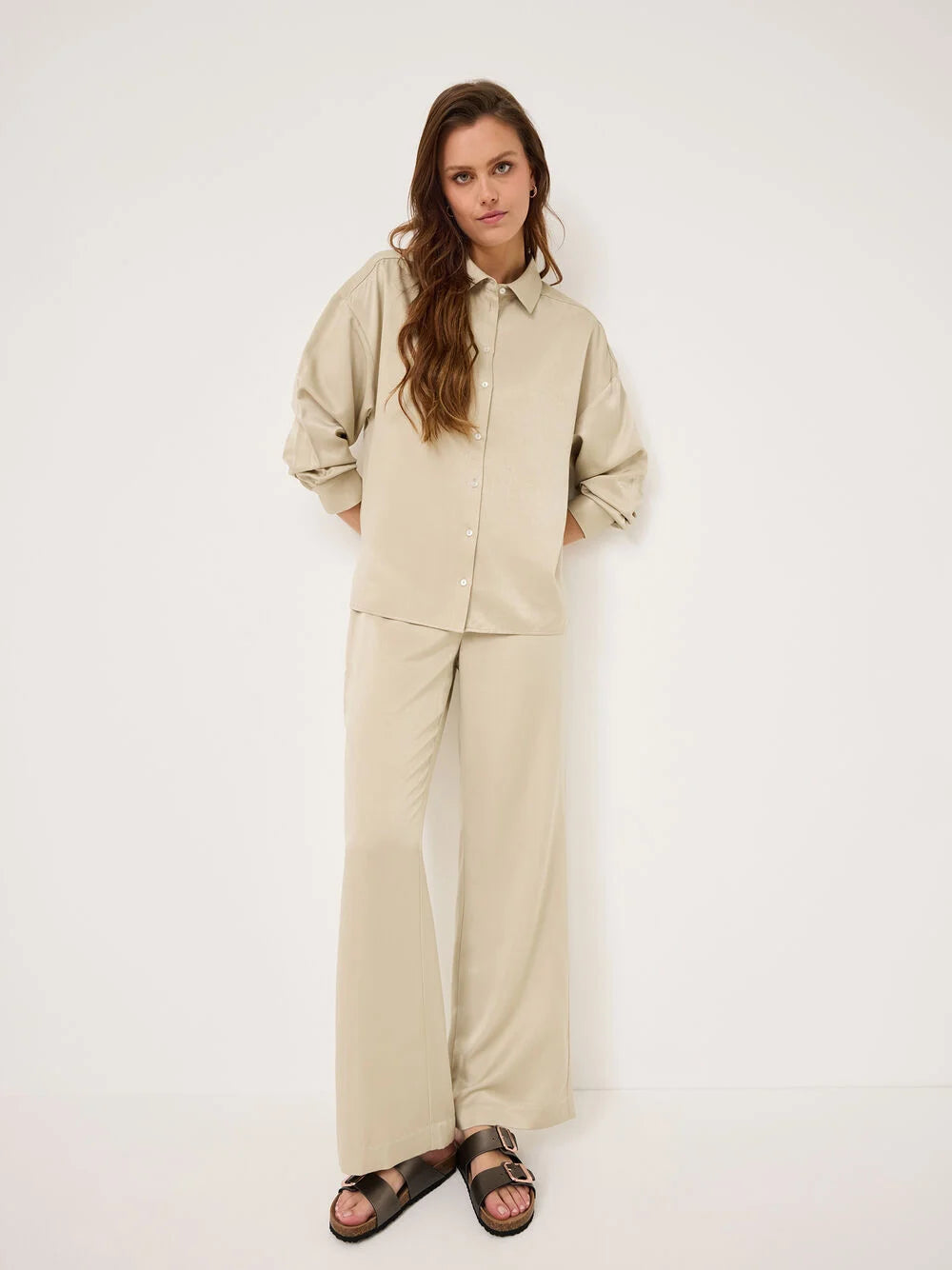 Woman wearing a beige shirt and pants set against a white background