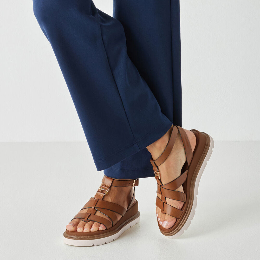 Brown sandals worn with blue pants on a light gray background