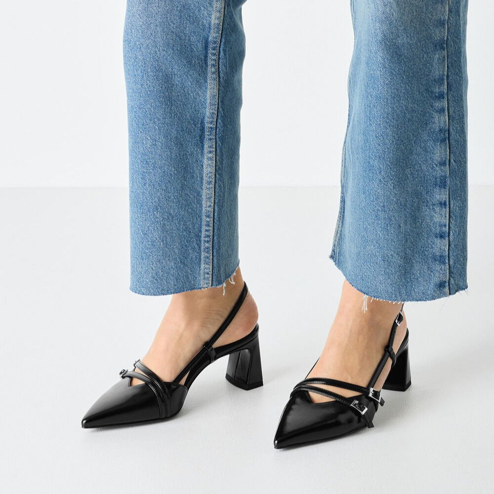 Black pointed-toe shoes with straps worn with blue jeans on a white background