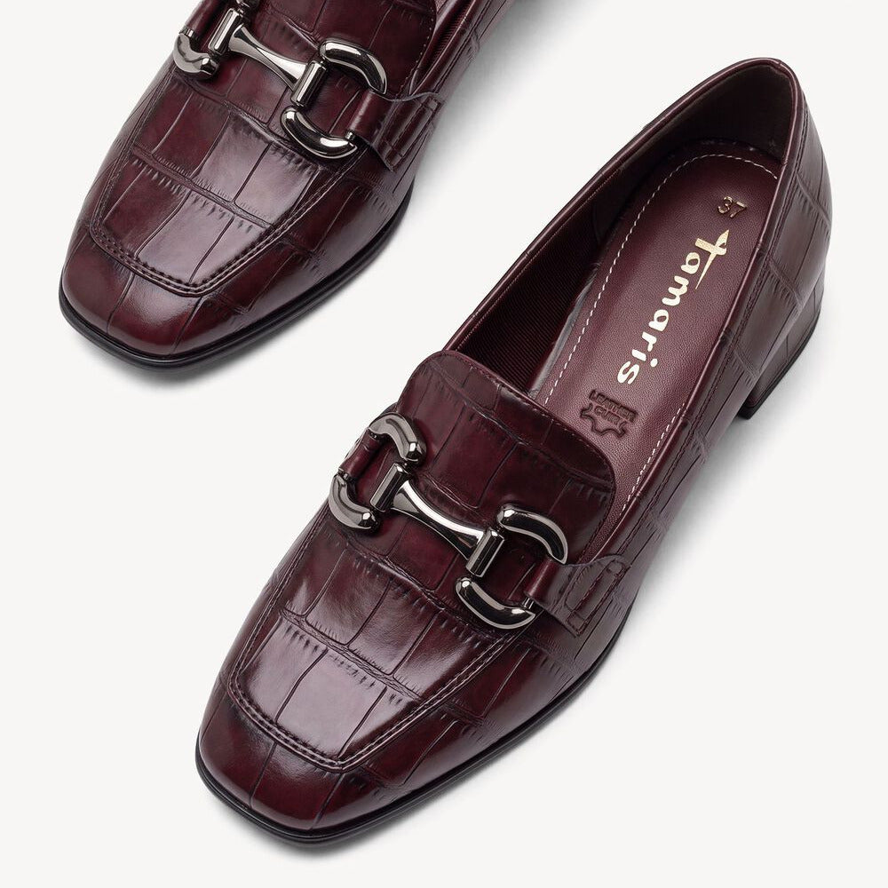A pair of women's burgundy crocodile-embossed leather loafers with silver horsebit hardware, shown from a top-down angle on a light gray background.
