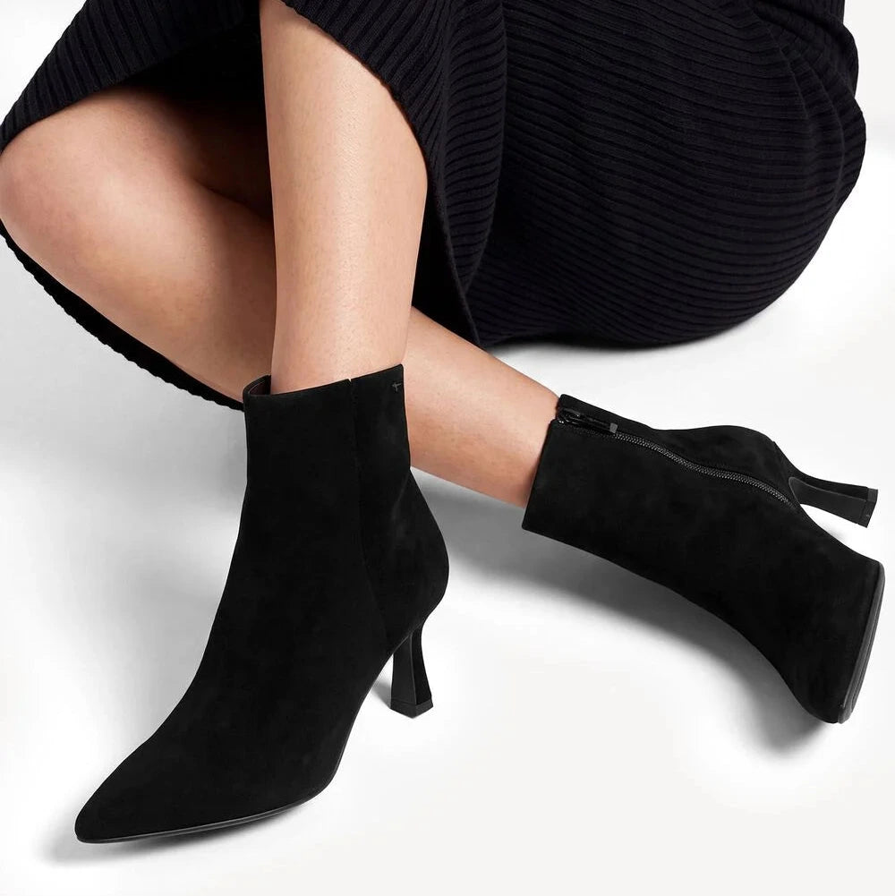 Black pointed-toe ankle boots with mid-height stiletto heels, shown on a model wearing a black ribbed midi dress against a white studio background.