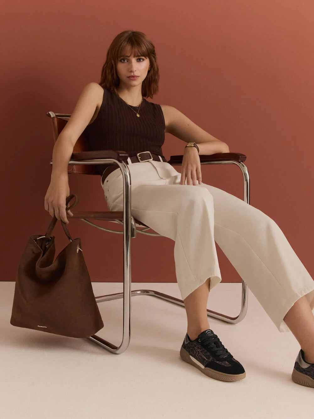 Woman sitting on a chair holding a brown handbag against a brown background