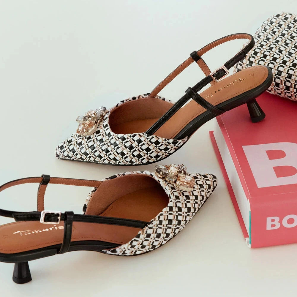 Pair of black and white patterned high-heeled shoes on a light surface with a pink box in the background.