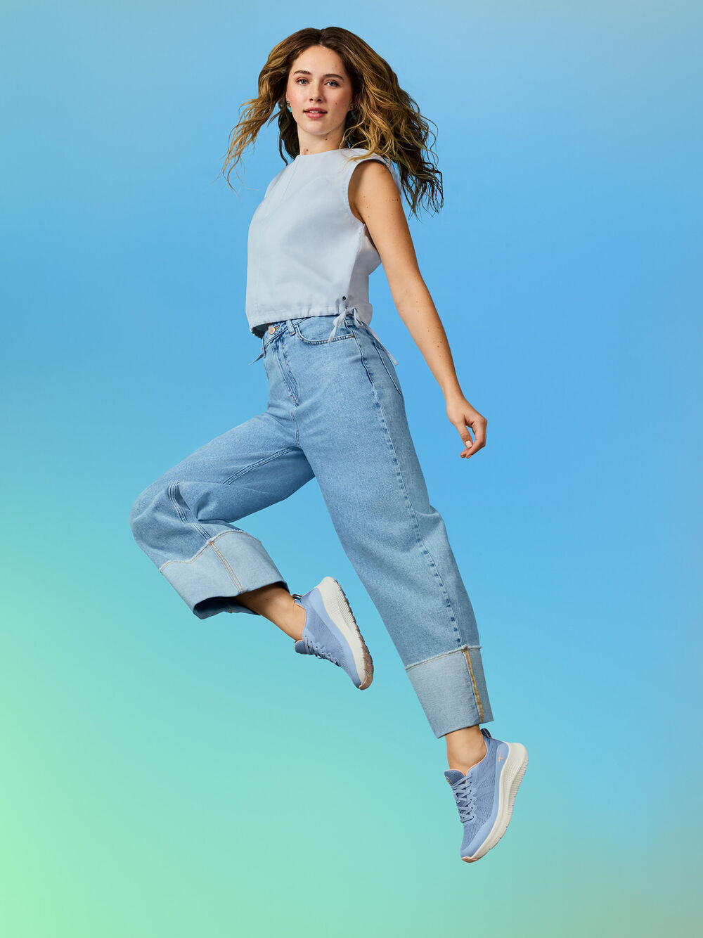 Woman in light blue top and jeans jumping against a gradient blue background