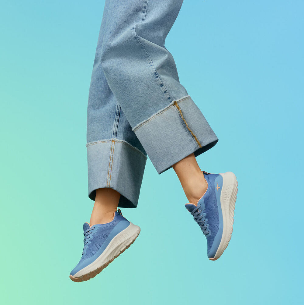 Person wearing blue jeans and matching sneakers on a gradient background