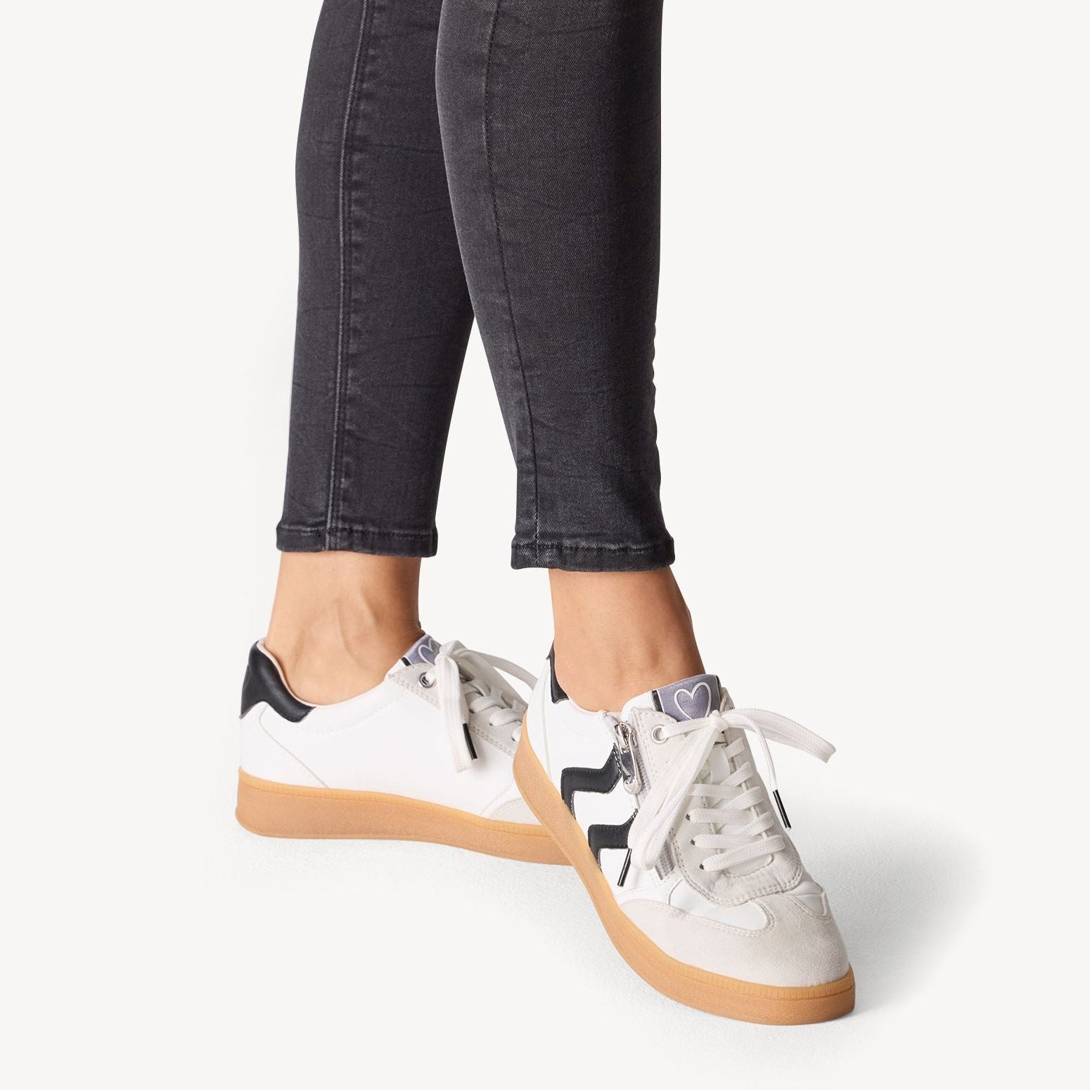 White sneakers with black star design worn with dark jeans on a white background