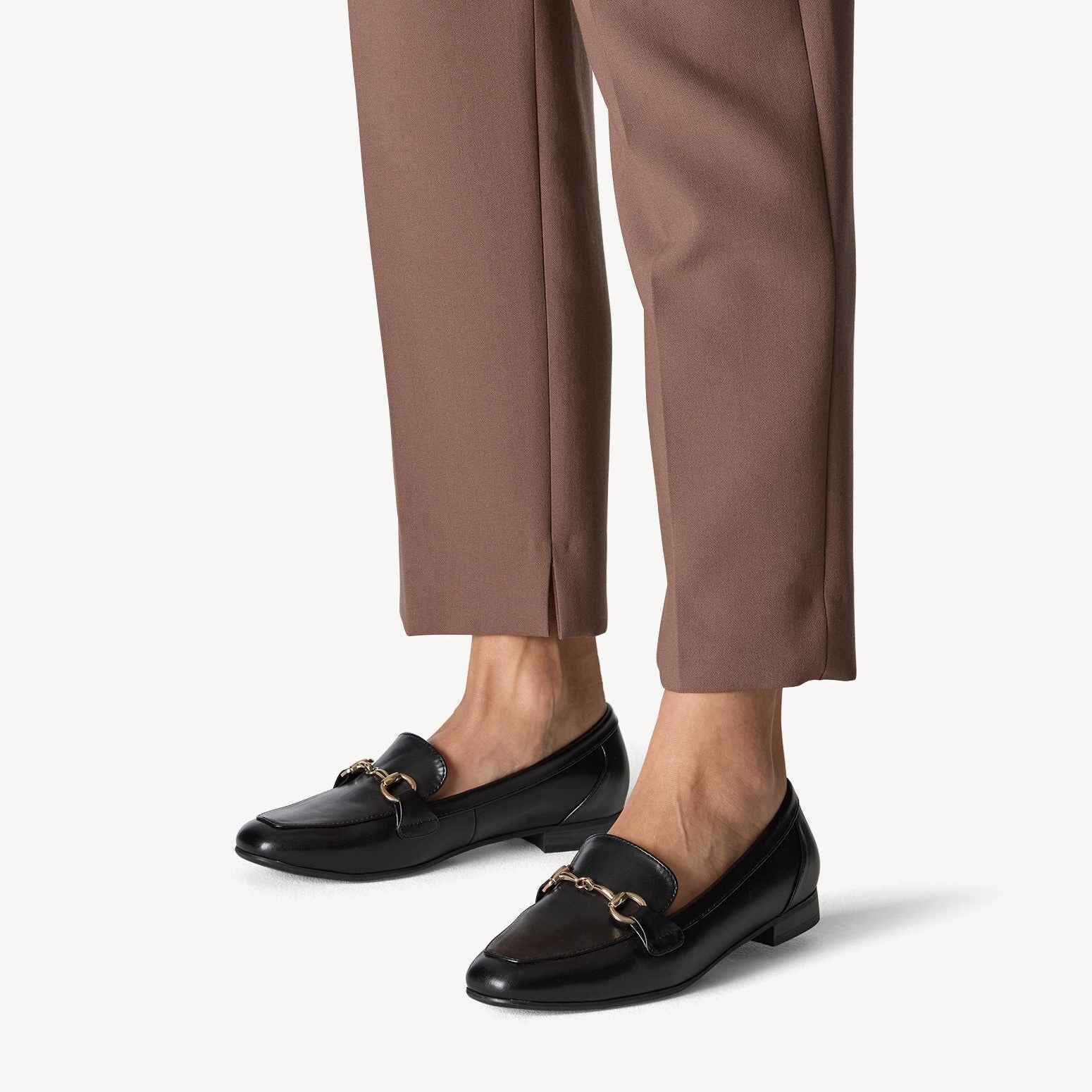 Black loafers worn with brown pants on a white background