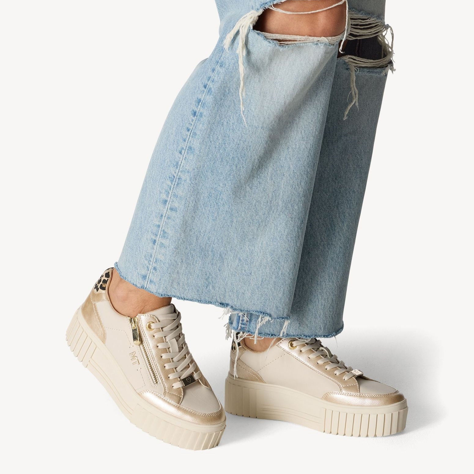 Person wearing light blue jeans and beige sneakers on a white background