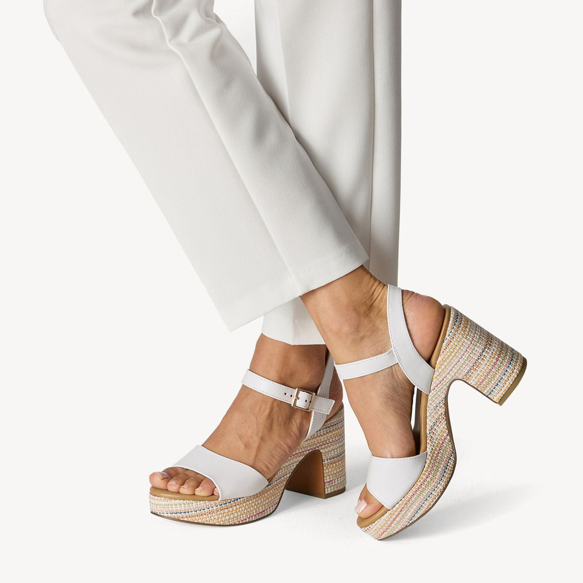 White sandals with wooden soles worn with white pants on a light background