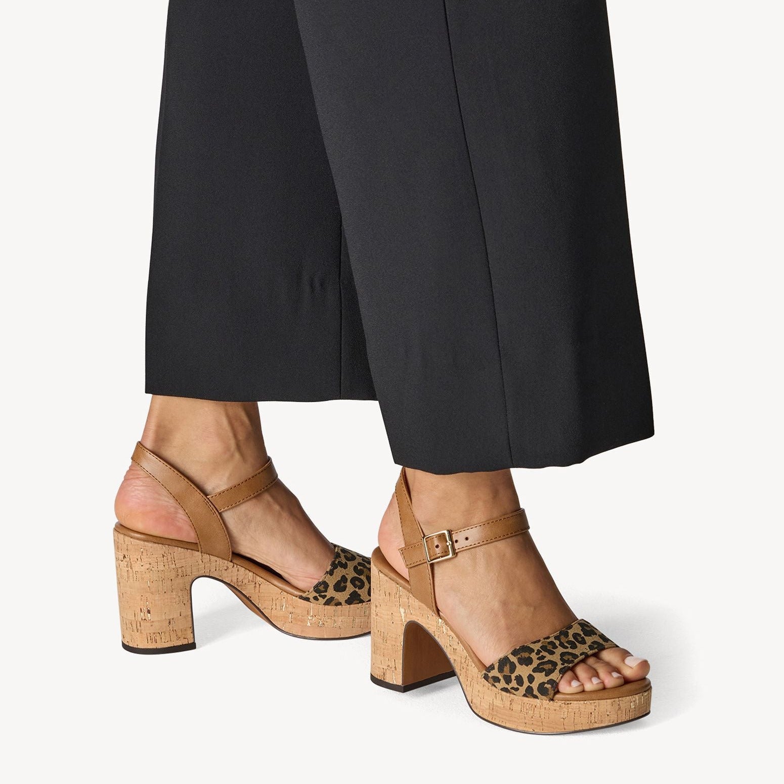 Brown cork sandals with leopard print straps worn with black pants on a white background