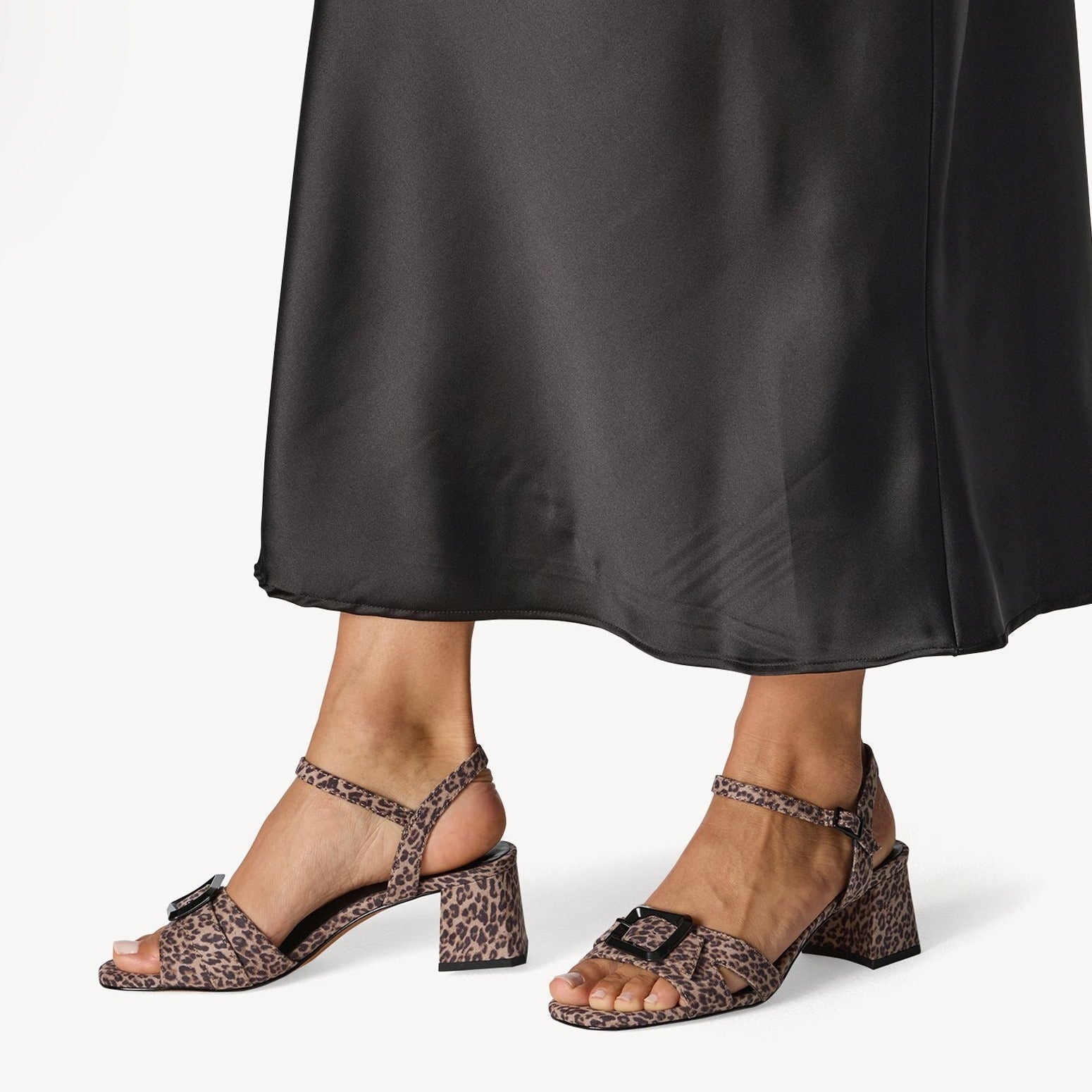 Leopard print sandals worn with a black satin skirt on a white background