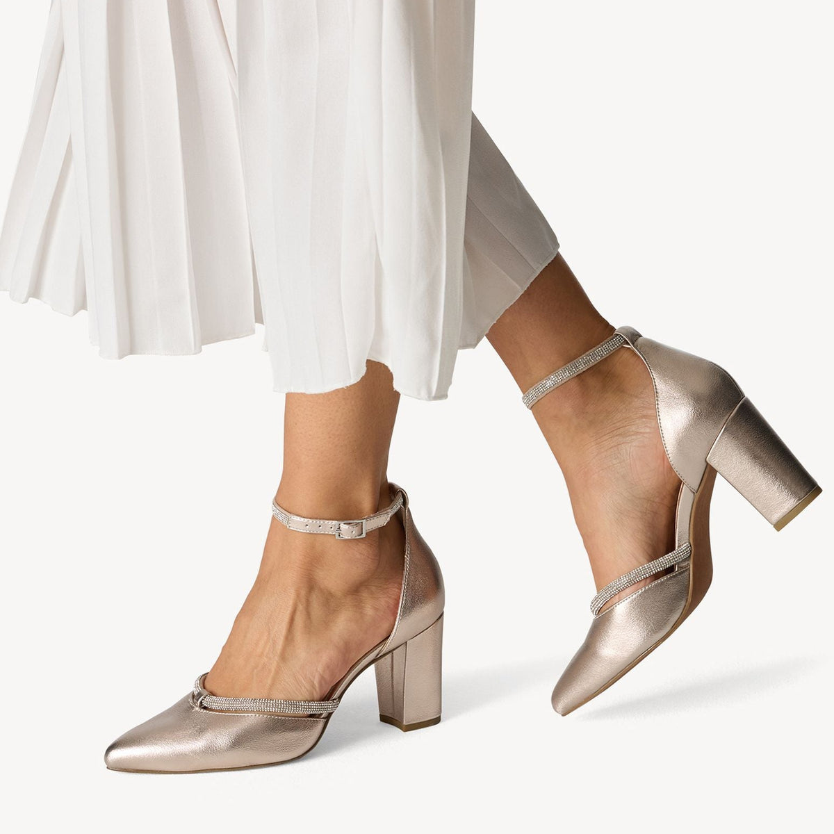 Metallic high-heeled shoes worn with a white skirt on a white background