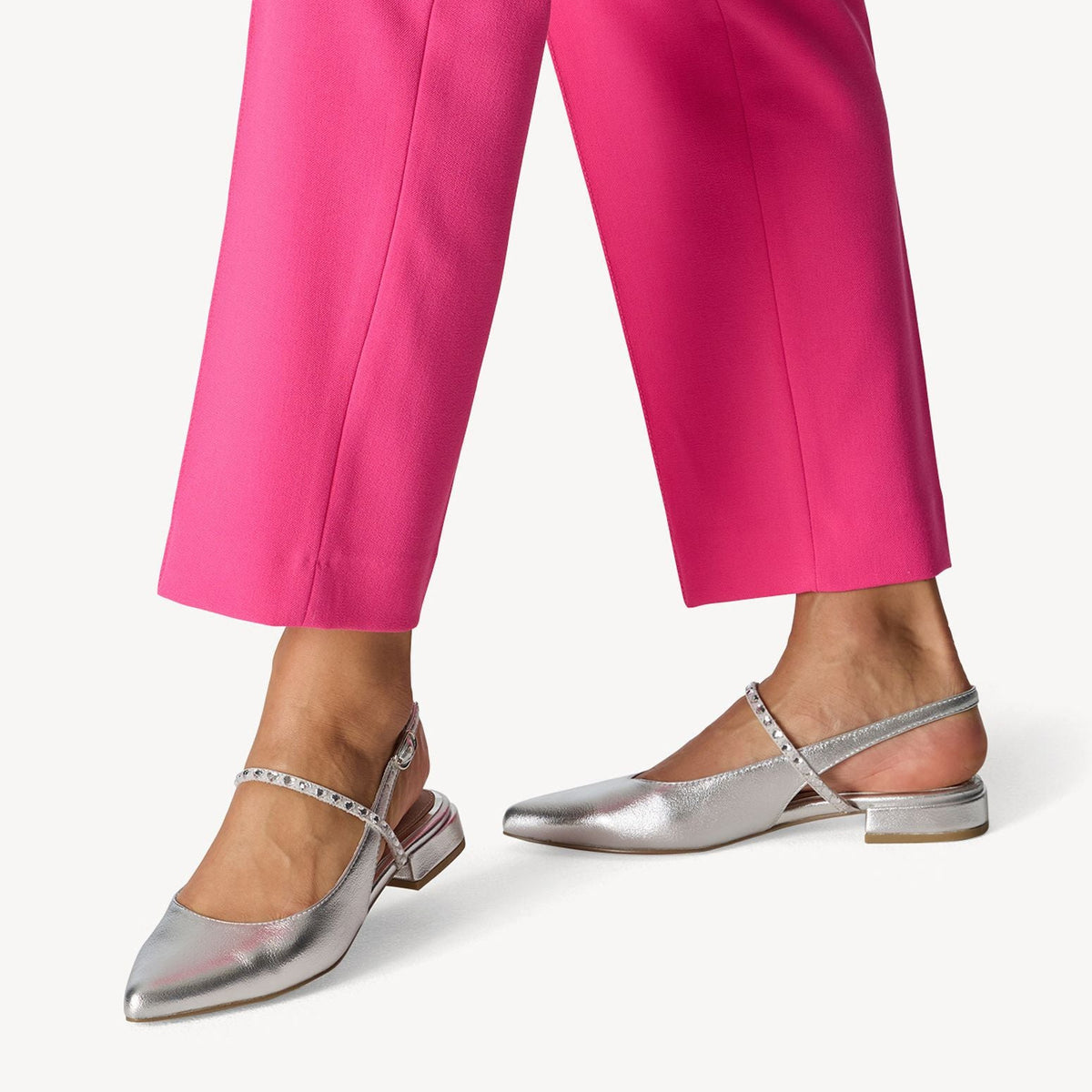 Silver pointed-toe flats worn with bright pink pants on a white background