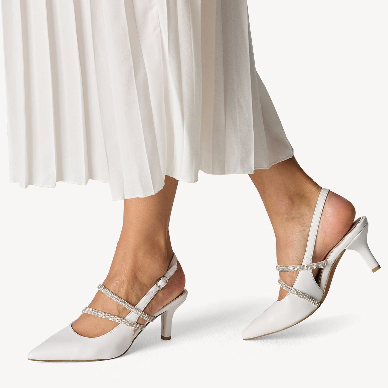 White high-heeled shoes worn with white pants on a light background